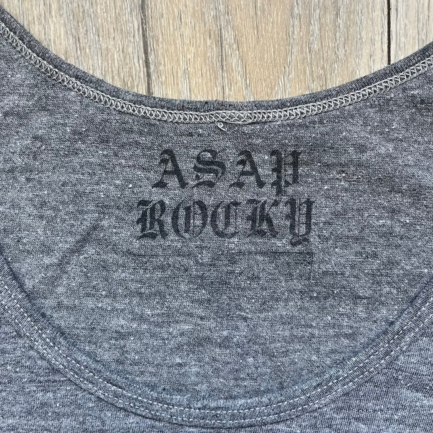A$AP Rocky 2012 “Peso” Gray Tank Top is a grey sleeveless shirt sold at concerts during the early A$AP Rocky tours. The front features stacked text reading “I be that pretty mother fucker” arranged word-by-word from top to bottom, followed by a line and “ASAP Rocky” beneath. The neckline includes A$AP Rocky branding printed on the tag area.