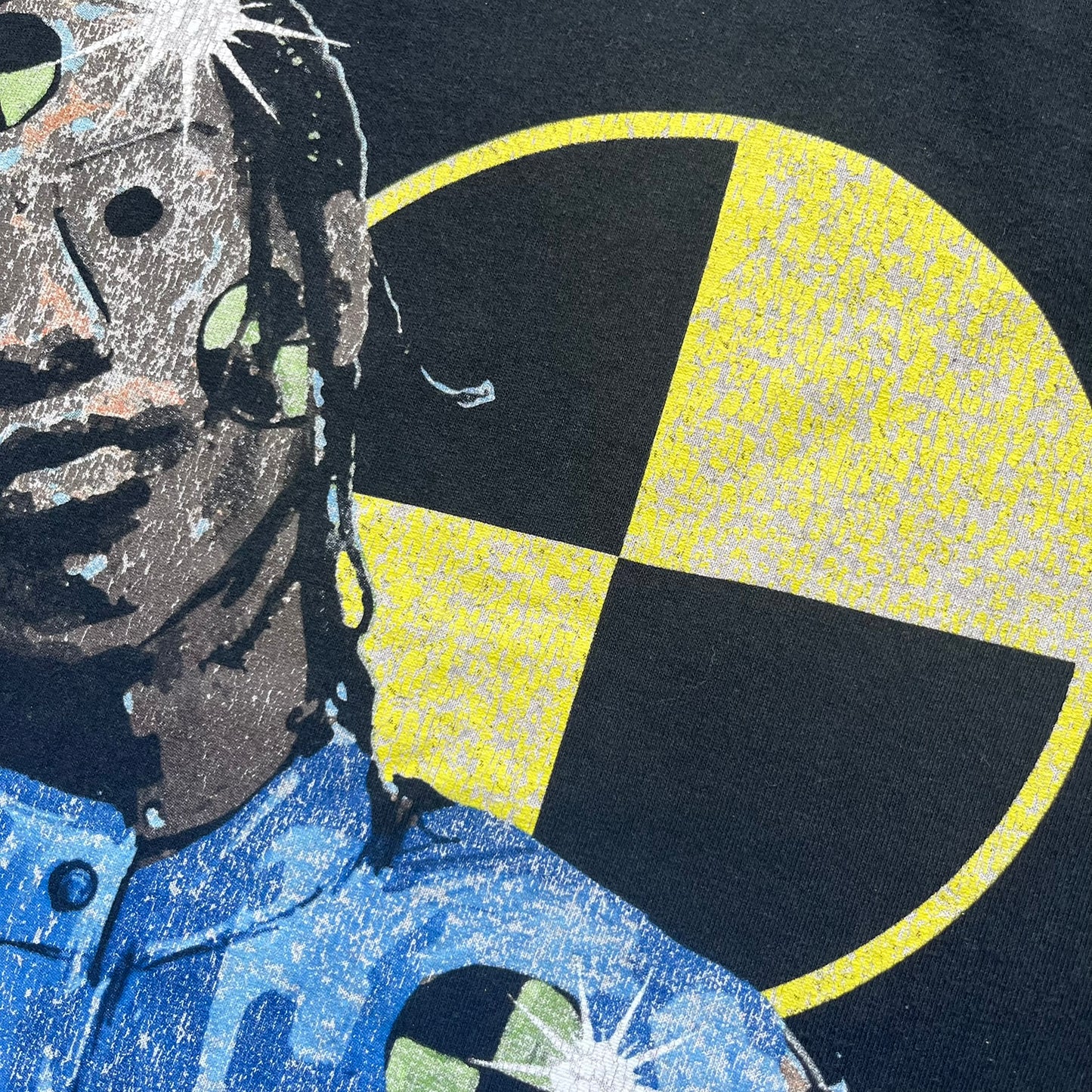 A$AP Rocky 2019 Injured Generation Tour “Crash Dummy” Tee is a black T-shirt released as part of the Injured Generation tour merchandise collection. The front features an illustrated crash dummy version of A$AP Rocky with “TESTING” text printed underneath. The opposite side includes a yellow and black burning TESTING logo graphic. Made in the USA. 