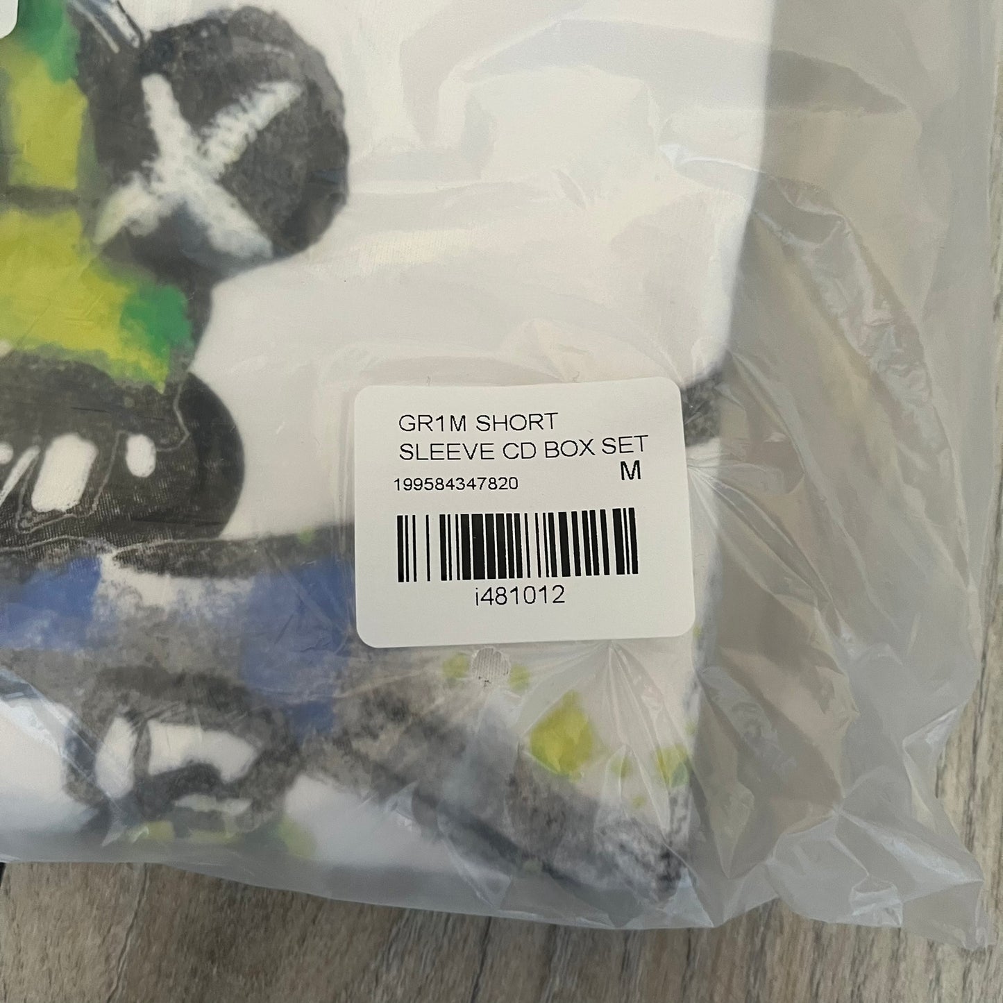 A$AP Rocky “Don’t Be Dumb” GR1M Short Sleeve Tee is a limited release from the AWGE website tied to the rollout of Don’t Be Dumb by A$AP Rocky. The white T-shirt features a green GR1M figure with a megaphone printed on the front with “GRIM” text below. The reverse includes a framed graphic with “Don’t Be Dumb” text, using a lenticular-style vinyl panel that shifts between the GR1M figure and A$AP Rocky in the same pose.