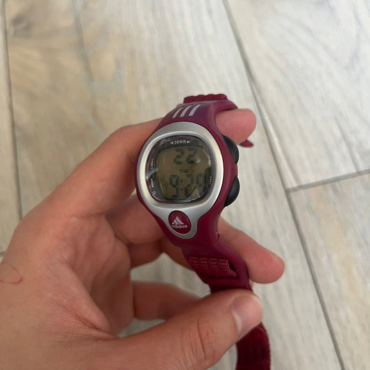 Adidas 2000s Burgundy 10-0117 Digital Watch (model X-003) is a burgundy digital watch with a silver bezel and ergonomic case. It features a burgundy nylon Velcro strap and four side buttons. The design includes three white stripes on the case and a silver Adidas logo button below the screen. The stainless steel back is engraved and marked water resistant up to 3 ATM, with an Adidas logo patch on the strap.