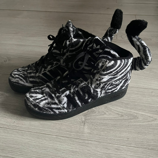 Adidas Jeremy Scott Zebra Black & White Sneakers – Sample pair, Style G95749. High-top sneakers featuring black and white faux-fur zebra print, a 3D tail at the heel, rubber soles, and front lace closure. From the FW13 Jeremy Scott for Adidas collection, these iconic sneakers combine classic adidas design with signature crazy JS styling. 