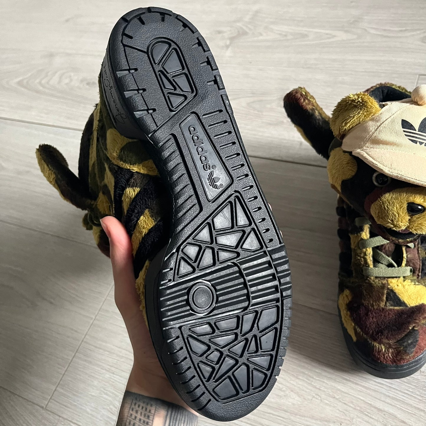 Adidas Jeremy Scott “Camo Bear” Sneakers (Style Q20917) released on March 16, 2013, in Earth Green/Black/Shioli. Featuring plush fleece uppers with a camouflage pattern, black three stripes, and a fully stuffed teddy bear head and arms on the tongue. Includes Jeremy Scott signature detailing on the inside heel and a black rubber sole.