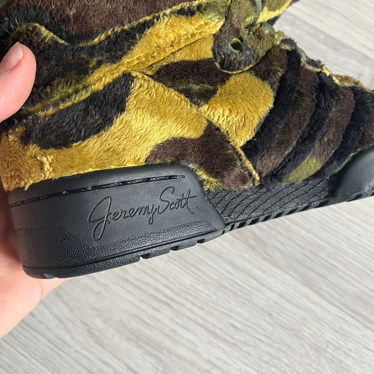 Adidas Jeremy Scott “Camo Bear” Sneakers (Style Q20917) released on March 16, 2013, in Earth Green/Black/Shioli. Featuring plush fleece uppers with a camouflage pattern, black three stripes, and a fully stuffed teddy bear head and arms on the tongue. Includes Jeremy Scott signature detailing on the inside heel and a black rubber sole.