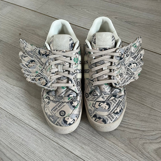 Adidas Jeremy Scott x Forum Wings 1.0 Low Money, style GX6393, in a Bliss/Off White/Bliss colorway. This pair features a textile upper covered in Jeremy Scott’s signature currency-themed graphic, swapping George Washington’s portrait for his own. The iconic 3D wings sit on the side of the shoe, with embossed adidas branding and Scott’s signature on opposite panels. Built with an EVA wedge for lightweight cushioning and a durable rubber cup sole. First released on October 21, 2021.