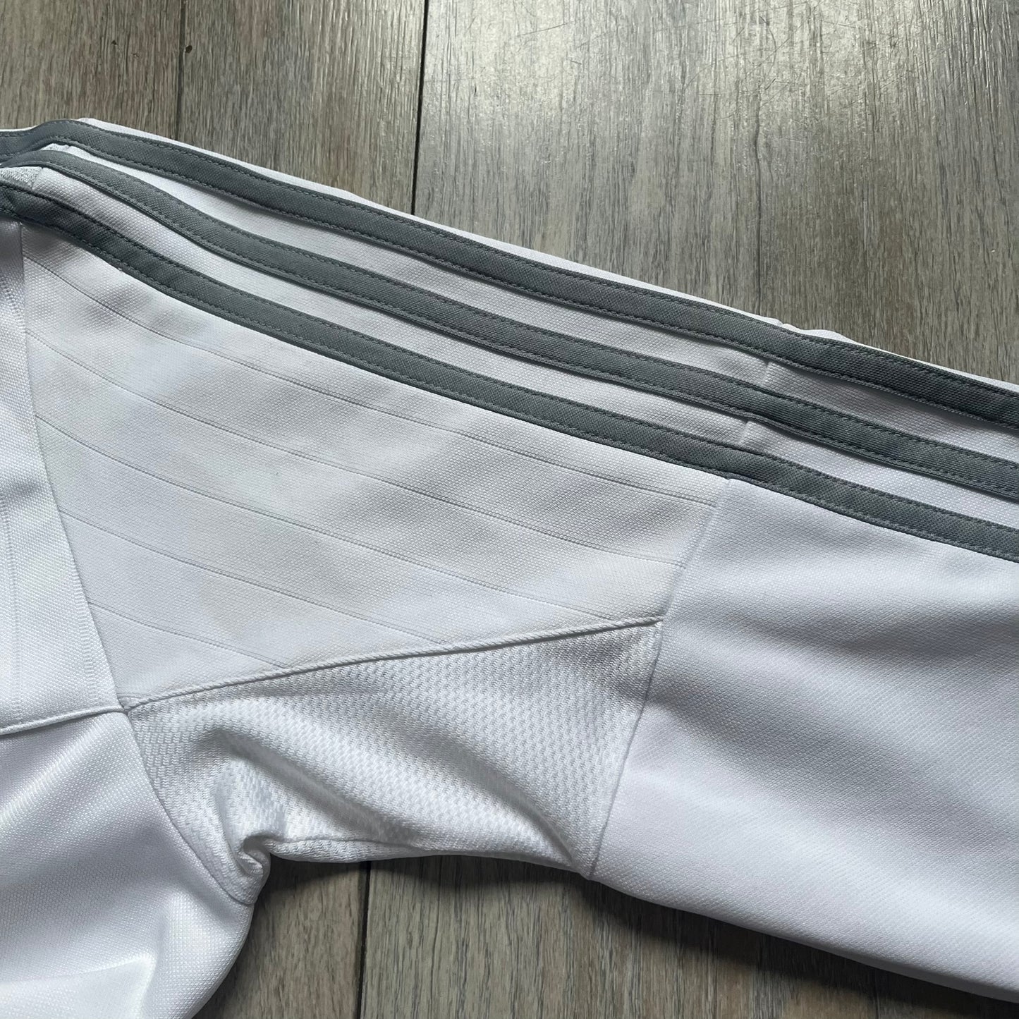 Adidas Talentförderprogramm Mercedes White Tracksuit is a white tracksuit featuring gray Adidas three-stripes running along the sleeves. The jacket displays Adidas, Mercedes, and Talentförderprogramm logos on the chest, with a white collar and a diagonal side zipper. Made with Climacool technology, it offers breathable performance for athletic wear.