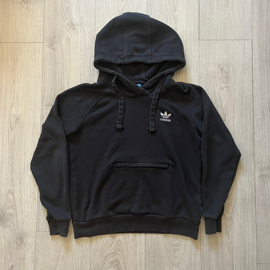 Adidas Trefoil Zip Pouch Hoodie in black, crafted from soft cotton for durability and comfort. Features a large Trefoil logo on the back within a circle, a smaller embroidered logo on the left chest, and a front zip pouch pocket. Designed with thick drawstrings and reinforced stitching, offering a sturdy, well-constructed fit.