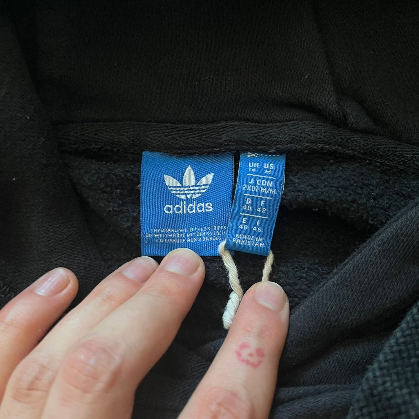 Adidas Trefoil Zip Pouch Hoodie in black, crafted from soft cotton for durability and comfort. Features a large Trefoil logo on the back within a circle, a smaller embroidered logo on the left chest, and a front zip pouch pocket. Designed with thick drawstrings and reinforced stitching, offering a sturdy, well-constructed fit.