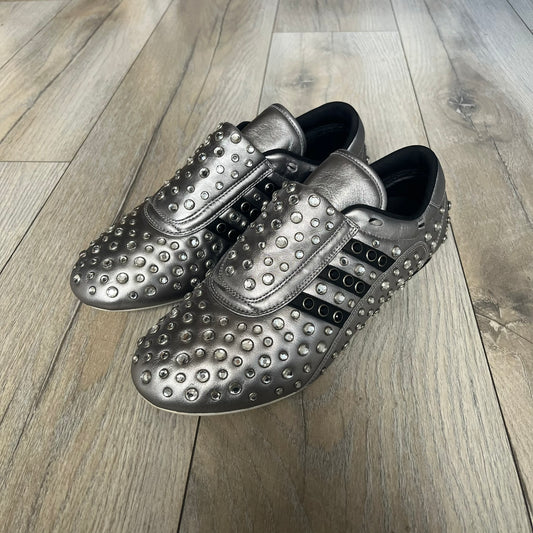 Adidas x Jeremy Scott 2010 Sample “Rockstar” Shoes (Article G16255) are a rare sample pair from the Spring/Summer 2010 collection, produced in June 2009. The shoes feature a metallic leather upper fully covered in circular rhinestone studs, with black Adidas three-stripe detailing on the sides and white soles. This model is built on a slim taekwondo-style silhouette and includes a yellow sample tag card.
