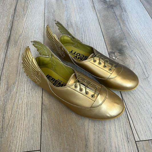 Adidas x Jeremy Scott 2011 Wings Gold Ballet Flats are a rare footwear design combining a classic ballet flat silhouette with Jeremy Scott’s signature wing motif. The shoes feature a fully metallic gold finish with visible stitching throughout the upper and wing construction. Small 3D wings extend from both sides of the heel area, creating the iconic Wings look in a streamlined form. Finished with a Trefoil Adidas logo on the back.