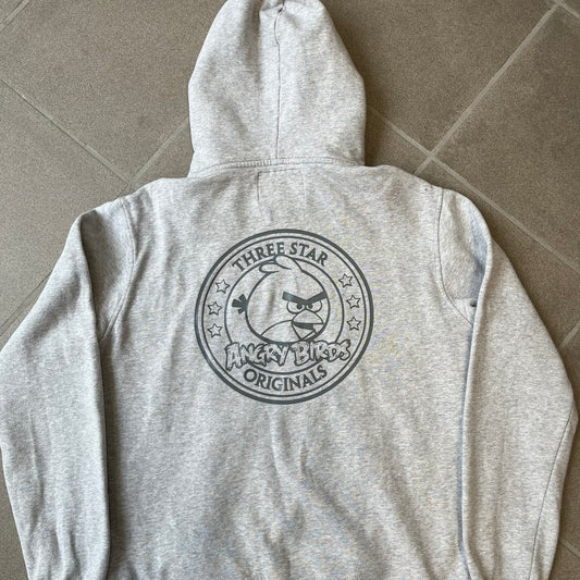 Angry Birds Three Star 2012 Foreman Pig Gray Hoodie features a grey hoodie design with a 3D-style front graphic of Foreman Pig, showing his recognizable eyes, nose, and mustache details. The back features a grey circular "Three Star" Angry Birds graphic, while the inside of the hood is finished with an orange lining.