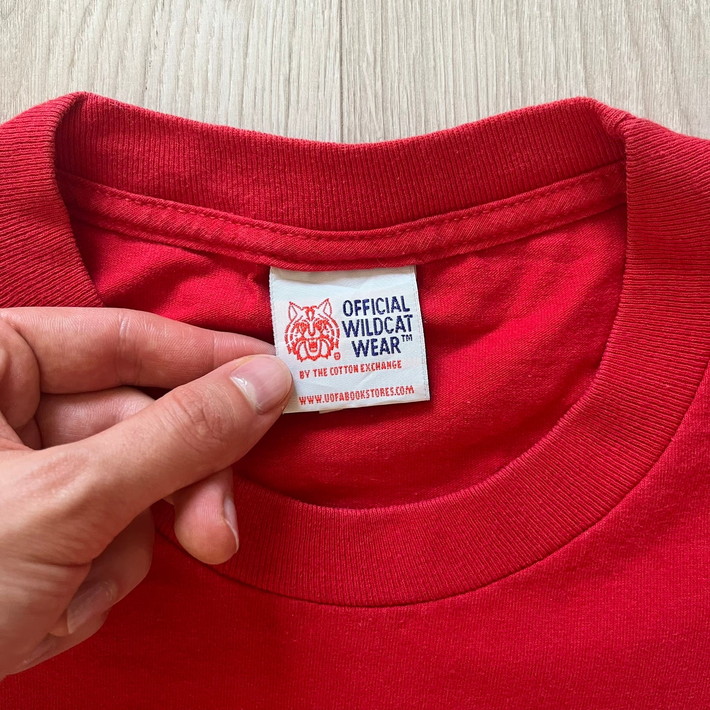 Red shirt with a visible label held by a hand on a light wooden surface