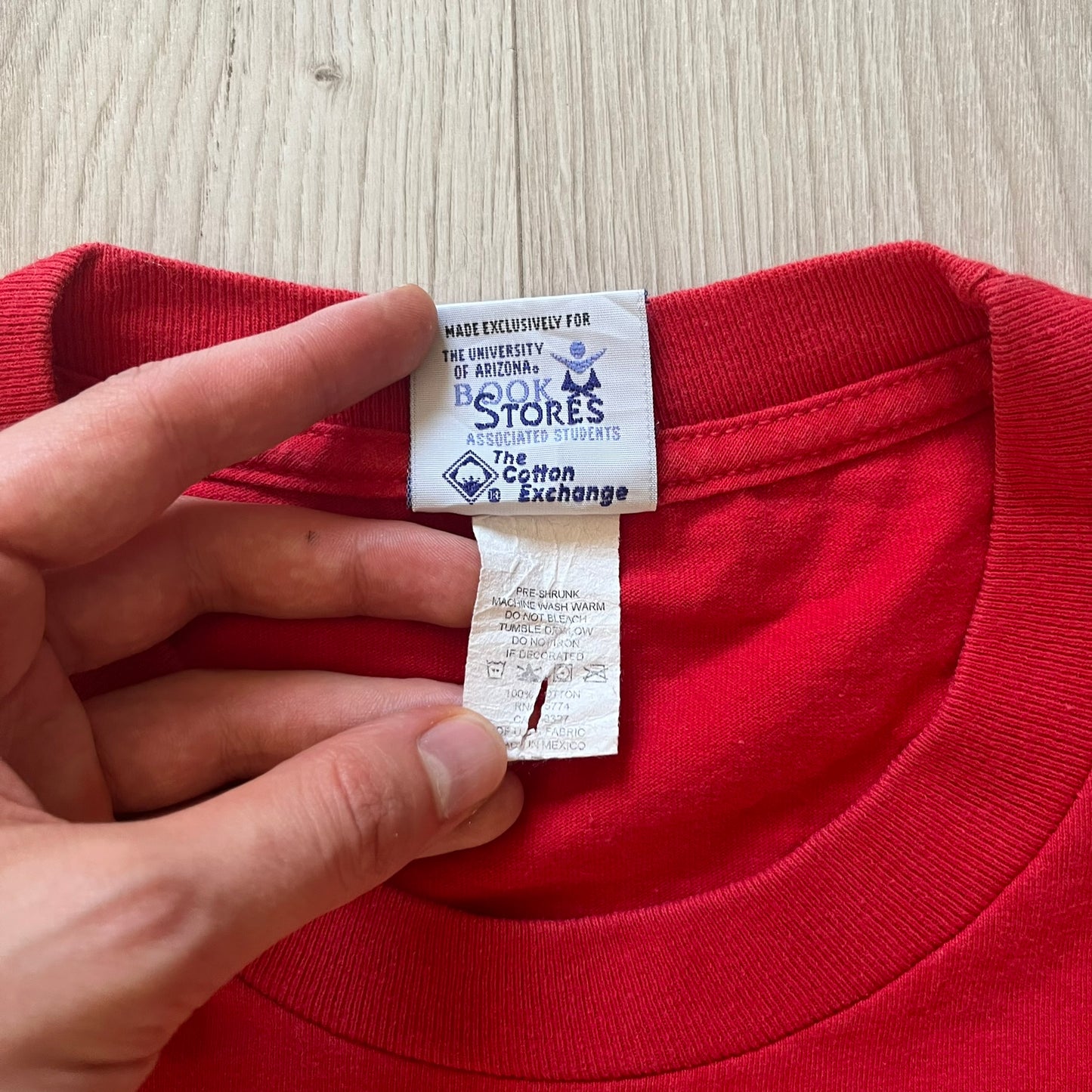 Red shirt with a tag held by a hand on a wooden surface
