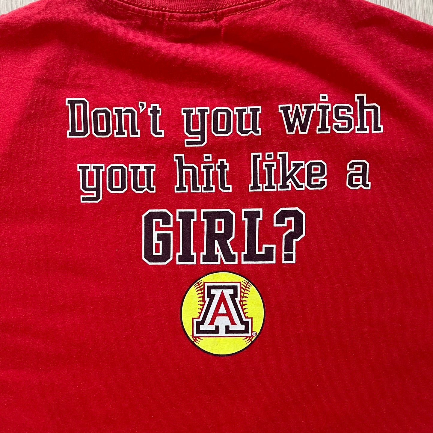 Red t-shirt with text 'Don't you wish you hit like a GIRL?' and a softball graphic on a plain background