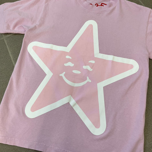 Asspizza 2025 Pink Star Tee is a dark pink T-shirt featuring a large light pink star graphic on the front. The star has a white outline and a white Happy Asspizza face design in the center. The shirt includes a red scribbled 2025 neck tag.
