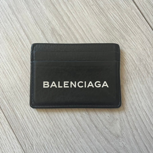 Balenciaga black leather card holder crafted in Italy from grained calfskin, featuring the updated Balenciaga logo in white inspired by public signage. Designed with four card slots and a central compartment, all fully lined in leather for durability. A sleek and practical accessory, it comes with a presentation box, reflecting Balenciaga’s modern luxury aesthetic under Demna Gvasalia’s creative direction.