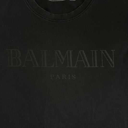 Balmain 2018 Black Tee featuring a discreet black Balmain Paris logo across the chest for a low-key, monochromatic effect. Constructed from soft 100% cotton and produced in Portugal, it embodies the brand’s modern, minimal direction.