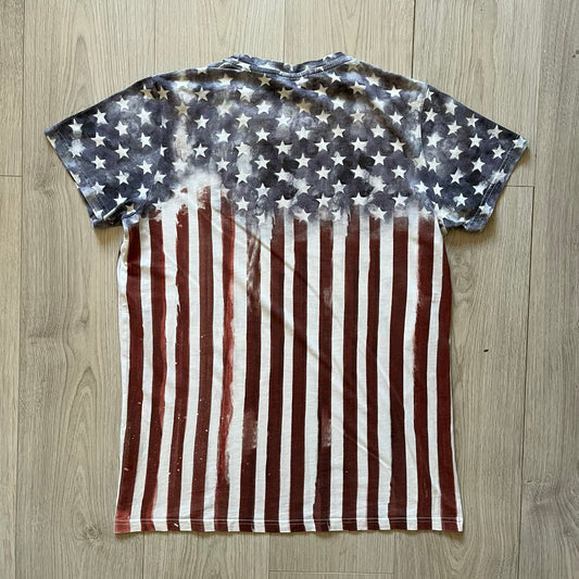 Balmain SS18 t-shirt in 100% cotton featuring a bold full-print USA flag on both sides. The front is accented with “Balmain Paris” text at the stomach, combining patriotic imagery with the brand’s signature luxury touch. A rare and powerful piece from the 2018 runway season.