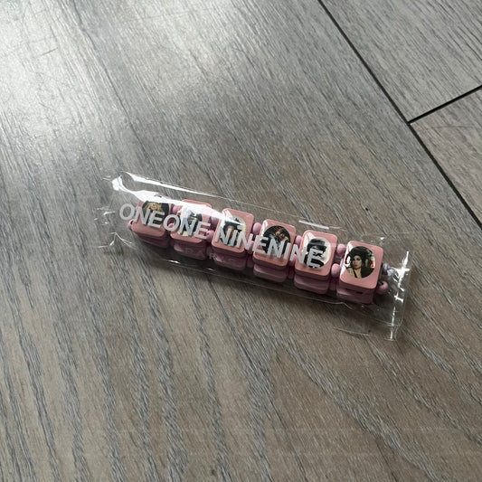 Blushing Bride “Forever 27 Club” bracelet by Bazo 1199, showcasing painted wooden beads and engraved portraits of legendary artists from the infamous 27 Club like Kurt Cobain, Basquiat, and Fredo Santana. Signed “forever 27 club” and “1199” on the inside.