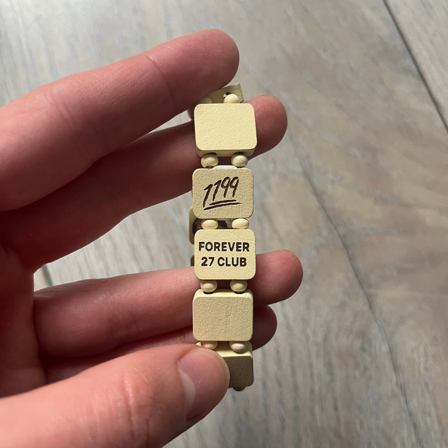 Pastel Yellow “Forever 27 Club” bracelet by Bazo 1199, showcasing painted wooden beads and engraved portraits of legendary artists from the infamous 27 Club like Kurt Cobain, Basquiat, and Fredo Santana. Signed “forever 27 club” and “1199” on the inside.