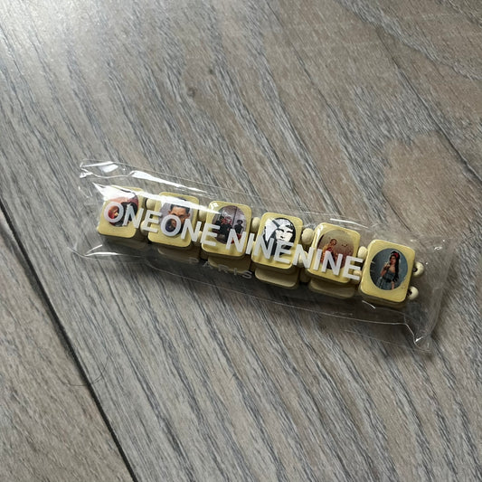 Pastel Yellow “Forever 27 Club” bracelet by Bazo 1199, showcasing painted wooden beads and engraved portraits of legendary artists from the infamous 27 Club like Kurt Cobain, Basquiat, and Fredo Santana. Signed “forever 27 club” and “1199” on the inside.