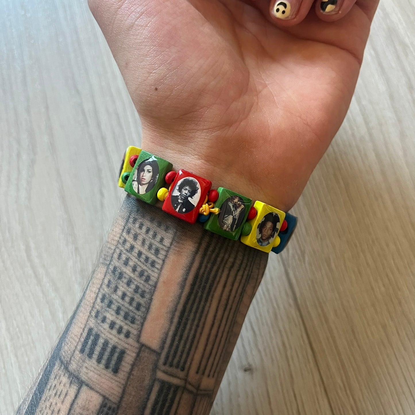Multicolor “Forever 27” bracelet by Bazo 1199, showcasing painted wooden beads and engraved portraits of legendary artists from the infamous 27 Club like Kurt Cobain, Basquiat, and Fredo Santana. Signed “forever 27” and “1199” on the inside, this piece is a striking nod to music and art history. Limited and highly sought-after, it captures both style and cultural significance.