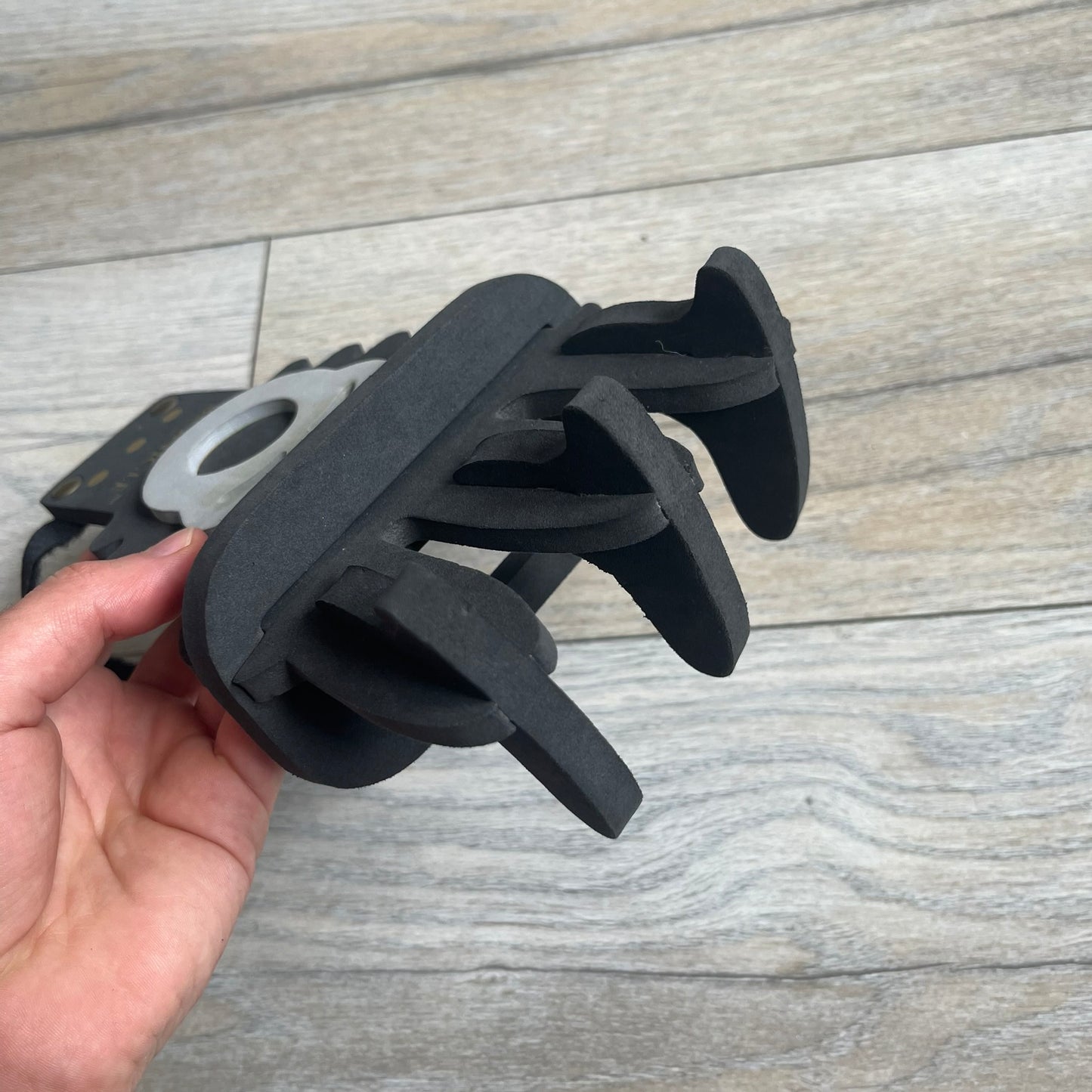 Bionicle 2000s Onua Foam Claw is a black and gray foam weapon featuring three claw tips at the top. It attaches to the wrist with a Velcro strap and is designed to be worn over the hand. The claw is marked with small gray LEGOLAND text and gold Bionicle branding near the bottom.