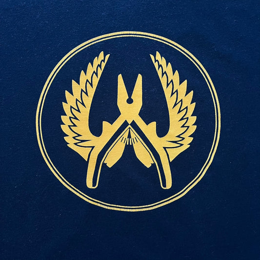 CS:GO 2015 Defuse Kit tee in navy, featuring a bright yellow defuse kit logo on the chest and a small yellow CS:GO patch on the sleeve. Made in Nicaragua from a 60/40 cotton-polyester blend, it includes licensed 2016 Valve Corporation and Counter-Strike Global Offensive tags. A collectible gaming tee that celebrates one of the most iconic in-game items from the series.