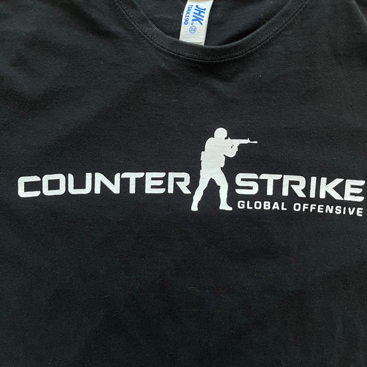 CS:GO Black & White Logo 2010's Tee is a black T-shirt made on a JHK blank. The front features a large white CS:GO logo with an armed figure and “Counter-Strike Global Offensive” text below. Super simple - classic CS logo.