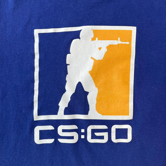 CS:GO Logo Navy Tee features a navy blue design with a large Counter-Strike: Global Offensive logo printed across the front. The graphic showcases the iconic navy, orange, and white CS:GO logo with the Counter-Terrorists silhouette above big white "CS:GO" text. Made from 100% cotton.