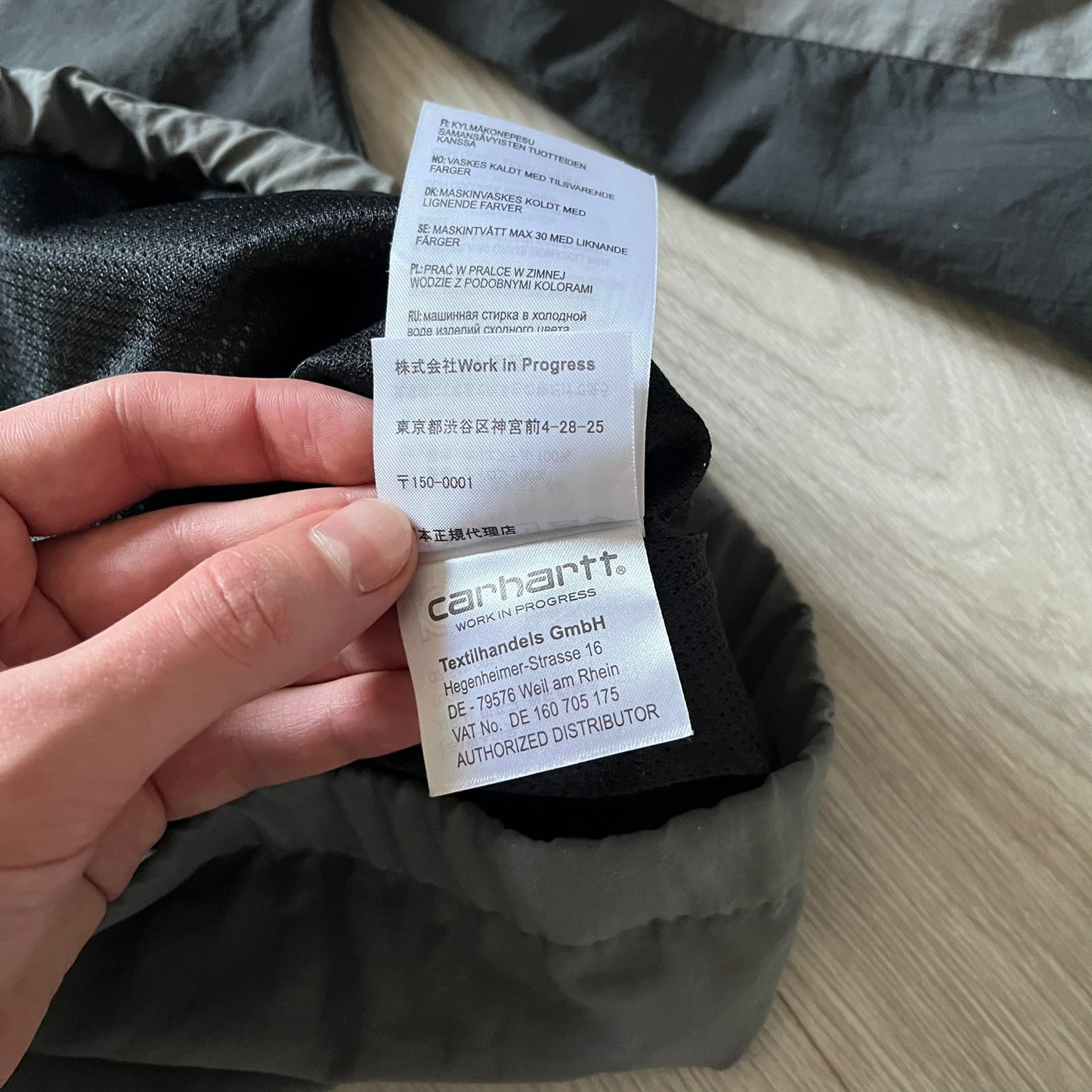 Carhartt WIP Gray Field Windbreaker featuring a dynamic two-tone design split diagonally across the body in light and dark gray. Crafted from durable nylon and polyester layers, it includes a small white Carhartt logo on the chest and large diagonal Carhartt embroidery on the back.