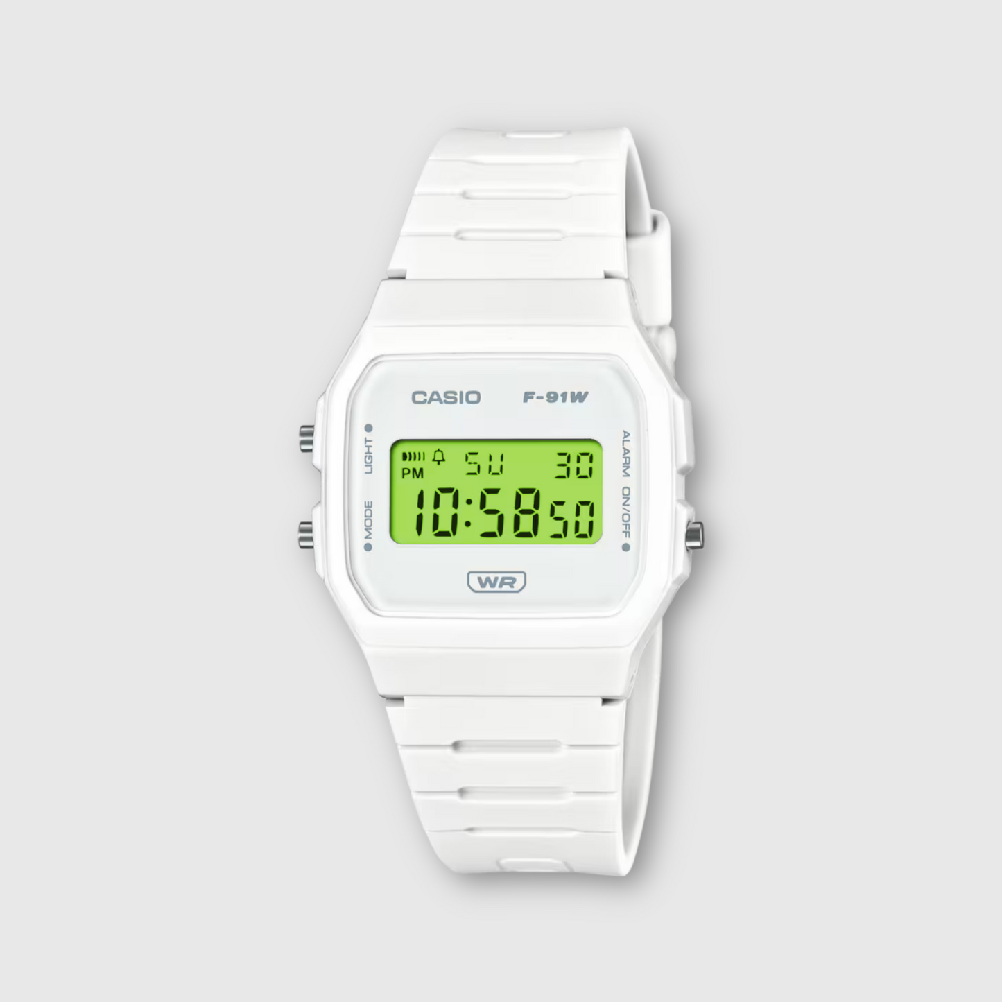White Casio digital watch with green display on a light gray background