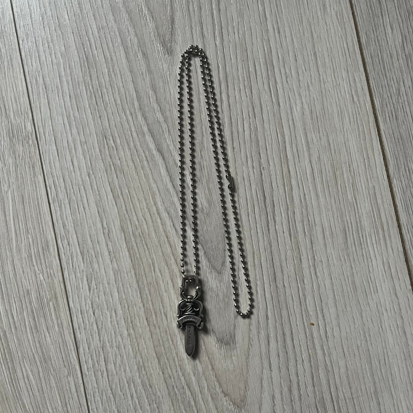 Chrome Hearts Dagger #10 Pendant crafted from genuine .925 silver, featuring the brand’s signature double-sided dagger design with “Chrome” on the guard and “Hearts” on the blade. Comes on a standard steel ball chain (non-CH). The top rectangular bail includes engraved markings: “89/03” on one side and “Sterling” on the other. 