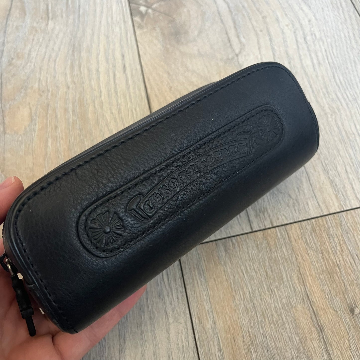 Chrome Hearts Hung Shield Black Sunglasses are black sunglasses from Chrome Hearts featuring black lenses and detailed metal hardware on the arms. The outer arm joints are finished with dagger emblems, while the inner sides feature Chrome Hearts cross motifs. The arm tips include metal end pieces with engraved Chrome Hearts branding. The pair comes with a black leather Chrome Hearts case.