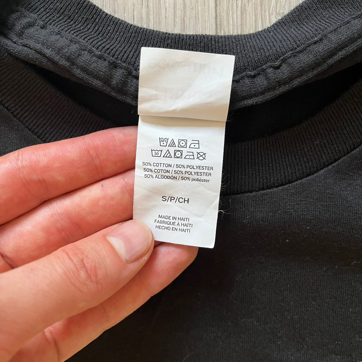 Clothing label on a black garment held by a hand