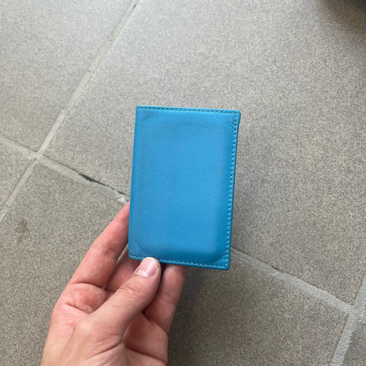 Comme des Garçons Blue Bifold Leather Wallet features a clean and minimal bi-fold design crafted from smooth aqua blue calf leather. The interior includes multiple card slots, a banknote compartment, and a gold-tone Comme des Garçons logo stamp for a subtle branded detail. A timeless everyday accessory combining practical organization with the brand’s signature minimalist aesthetic.