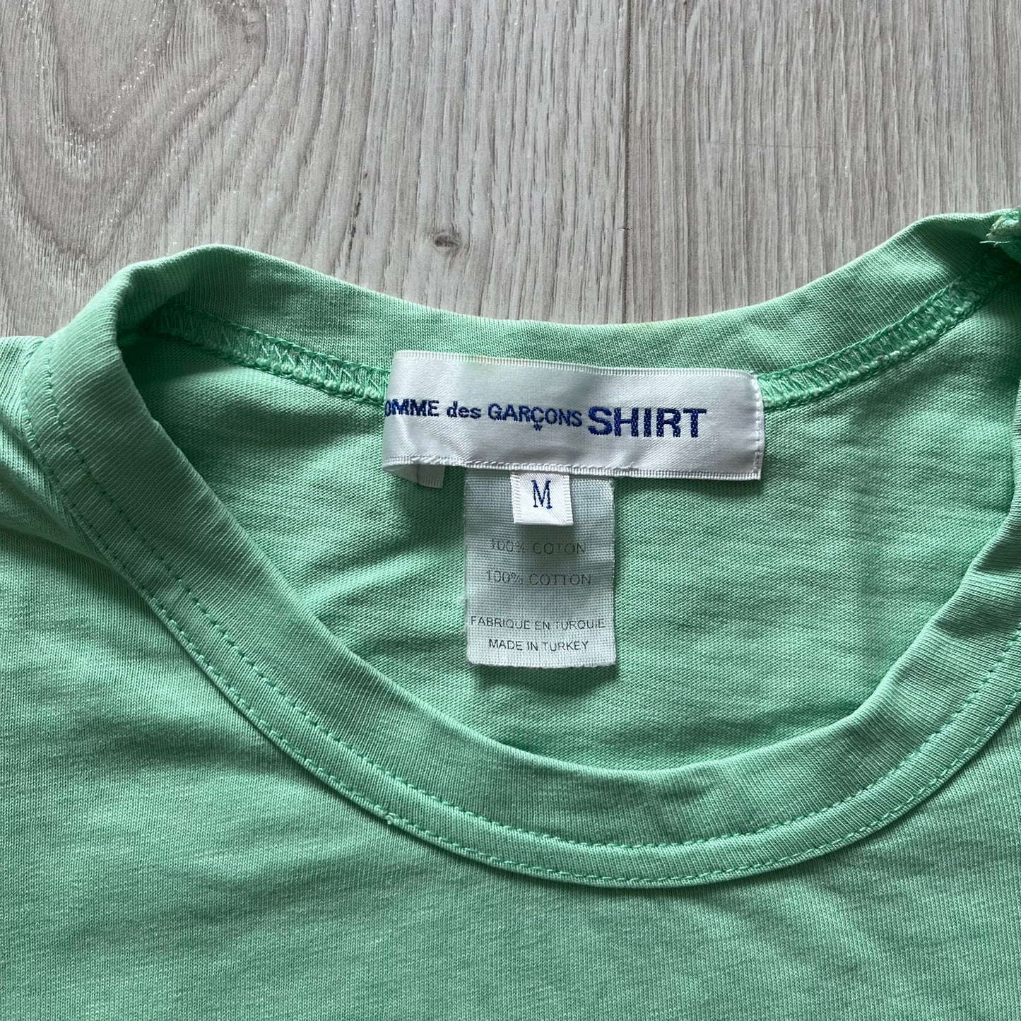 Close-up of a green shirt with a label on a wooden surface