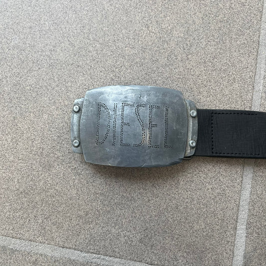 Diesel 2000s Vintage Buckle Leather Belt features a black leather strap made in Italy. The belt has a large rectangular metal buckle designed to look like a worn metal sheet, with a Diesel logo formed from small perforated holes. The buckle includes visible screws on the sides and the belt is made from 100% leather.