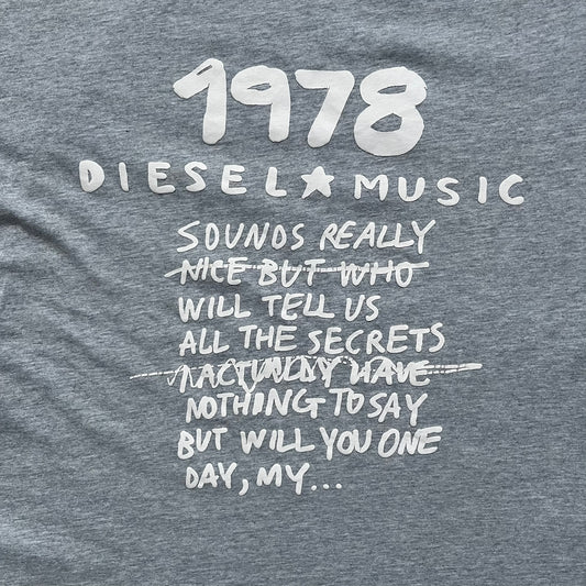 Diesel Music 1978 Gray Tee is a gray T-shirt featuring a large hand-drawn style “Diesel Music 1978” print on the front with additional text below. Made from 100% cotton, it has a crew neckline and short sleeves. The print is white, contrasting with the gray fabric.