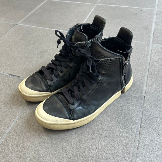 Diesel Zip-Round S-Nentish Black Sneakers feature a high-top silhouette with a black leather upper and a white rubber sole. The sneakers have a full-length zipper detail around the ankle area, running from the top of the shoe down and around the sides. The design includes a lace-up front and Diesel branding details.