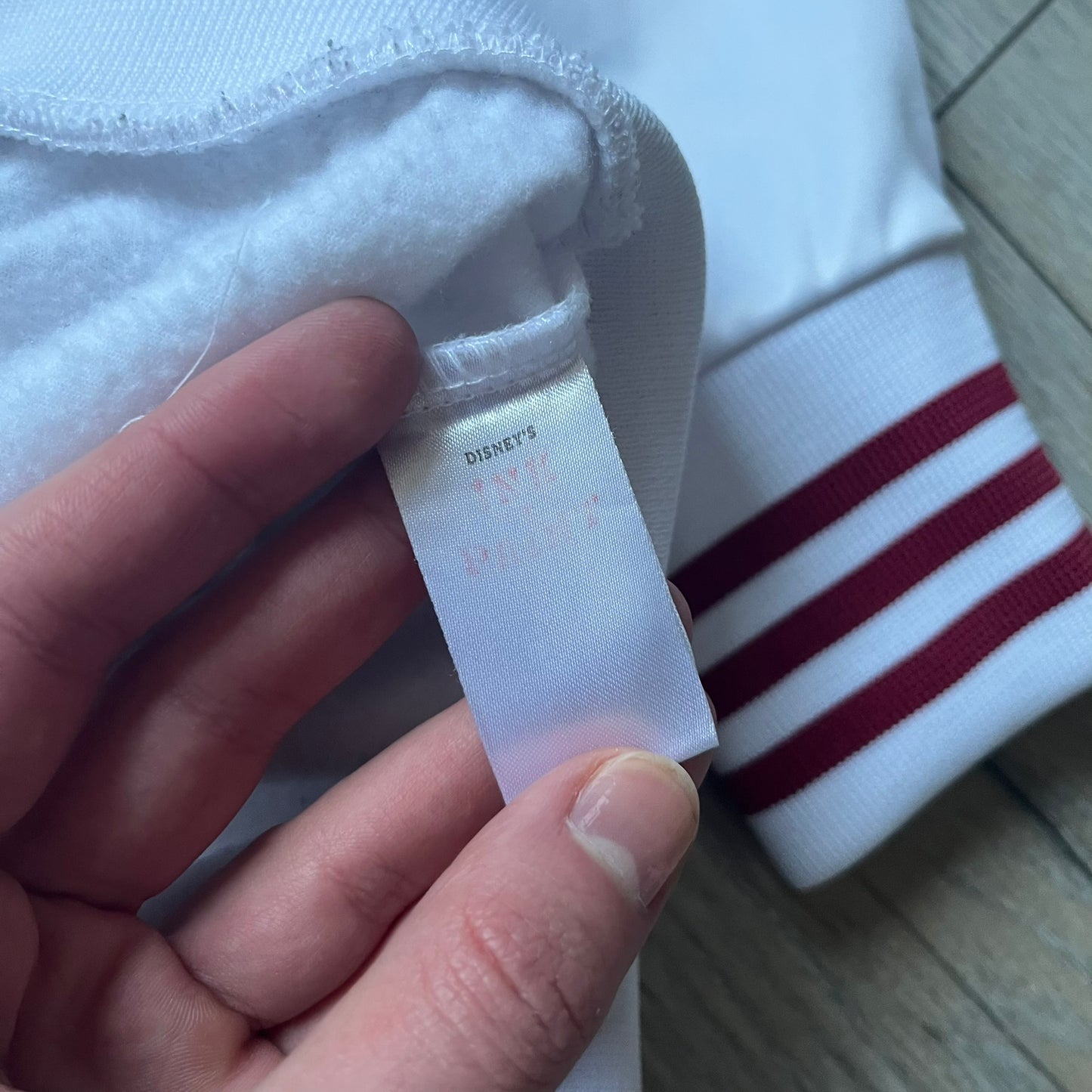 White 1990s Disney track jacket with red contrast details throughout. Features red stitching and accent lines, a red zip closure with a large red metal Mickey Mouse zipper pull, and a small Mickey Mouse face with red stars on the chest. The back has a large Mickey Mouse graphic with red stars and oversized “Tokyo” text printed above.