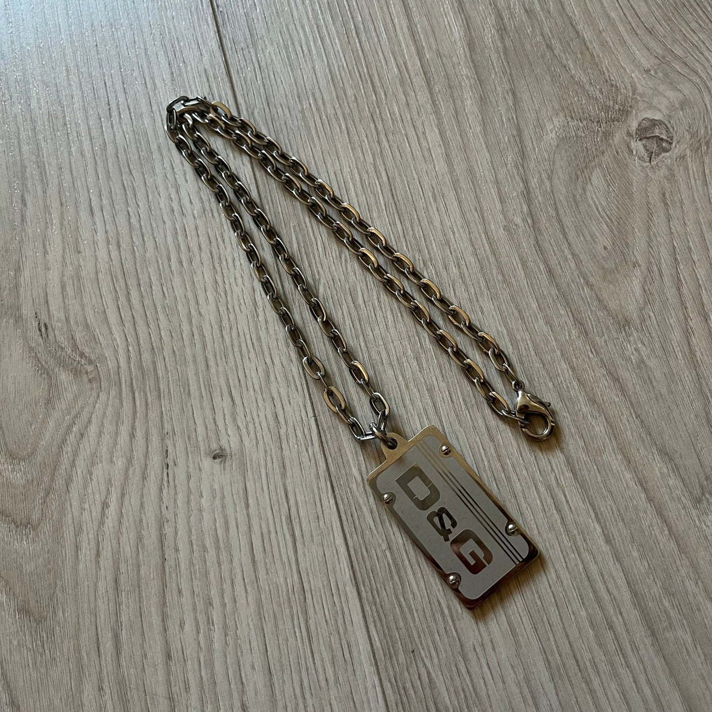 Dolce & Gabbana Propaganda Dog Tag Necklace, featuring a silver stainless steel square tag with four visible screws and the D&G logo engraved on the front. The tag hangs from a durable cable chain, combining sturdy construction with clean, industrial-inspired detailing.