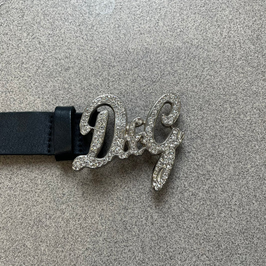 Dolce & Gabbana 2000s Black Crystal Buckle Belt features a black leather strap with a stainless steel D&G logo buckle. The buckle has a decorative italic-style font and is fully covered with crystal/rhinestone detailing on the front. Made in Italy.