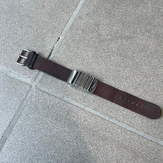 Dolce & Gabbana 2000's Brown Leather Bracelet features brown leather straps with an adjustable fit and a stainless steel central plaque. The plaque has a raised wavy texture on the front and a D&G logo underneath, while the leather straps have small D&G and “Genuine Leather” tags.