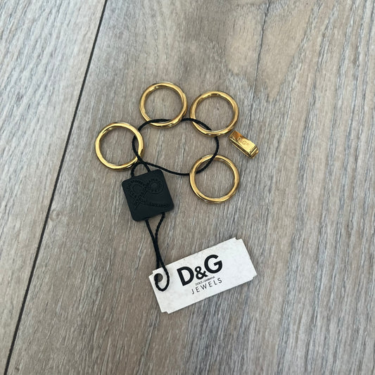 Dolce & Gabbana DJ0680 Gold Rings Set is a 2000s set consisting of four gold-tone rings. Each ring can be worn individually or connected together using the included square D&G clip to form a single four-ring design. The rings have a simple polished finish and come with the original tags.