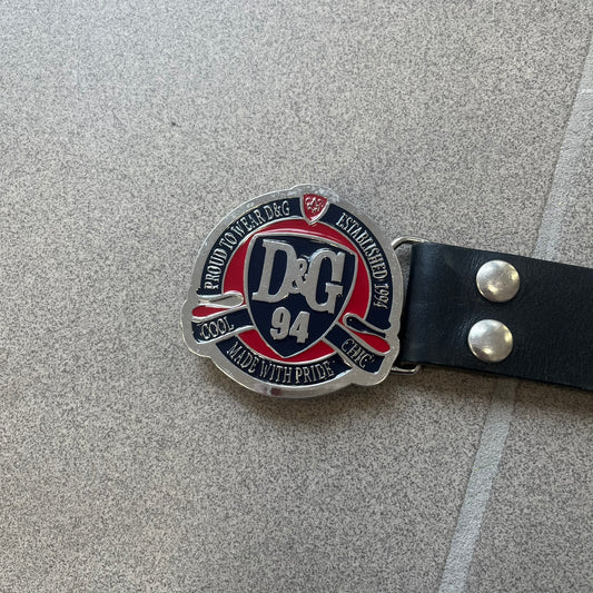 Dolce & Gabbana "Made with Pride" Belt features a circular silver buckle with D&G 94 at the center, surrounded by “Proud to Wear D&G,” “Made with Pride,” and “Established 1994” text. Finished with subtle red and navy accents, it comes with a non-D&G basic black leather belt.