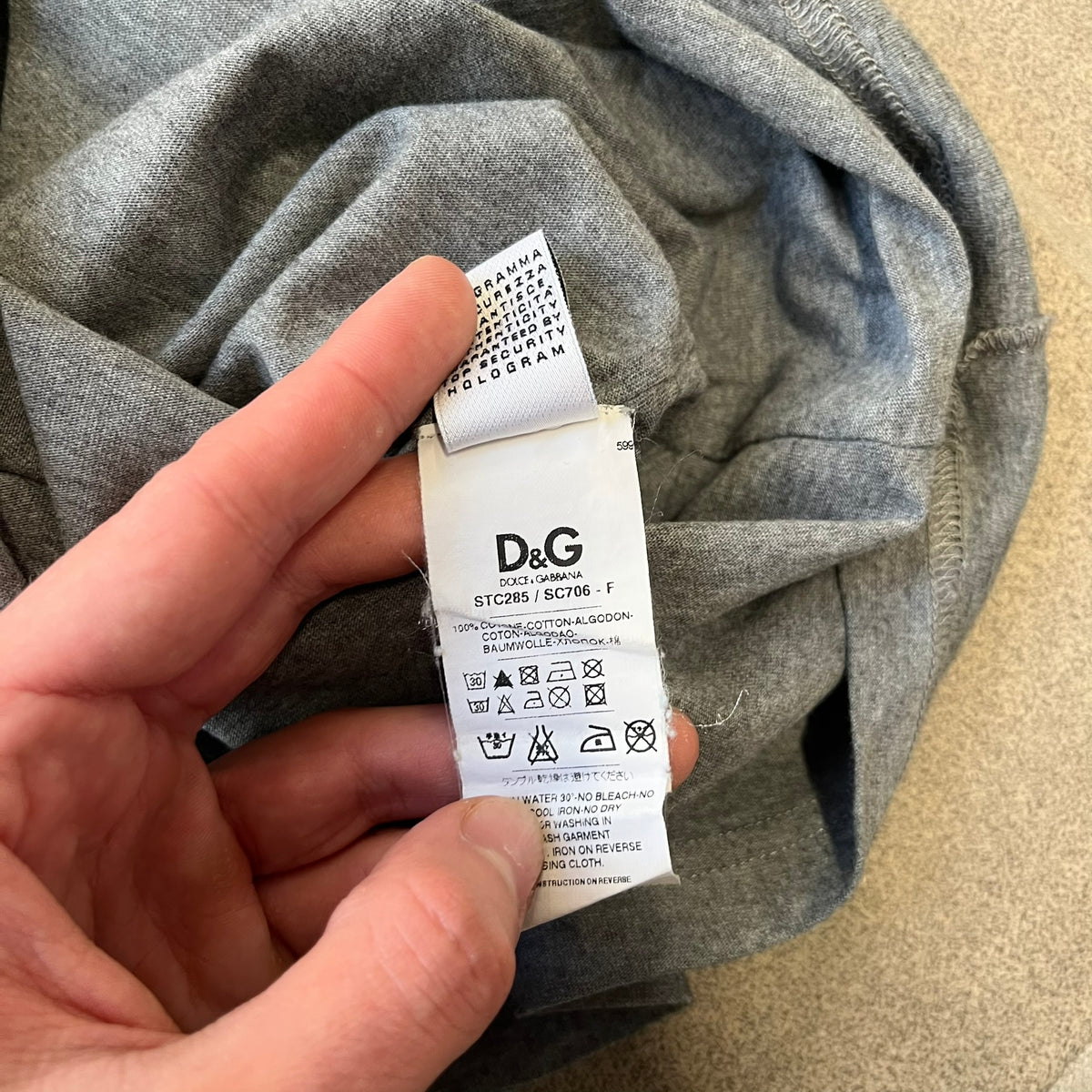 ● Dolce & Gabbana 2000's Photo by Mario Testino Tee is a gray T-shirt with a photo of Naked Man and Woman holding each other on the front, and small “Photo by Mario Testino” text below it. The upper back has “D&G 10 La Roue De La Fortune” text. The shirt is constructed inside-out style, with the stitching visible along the sides.