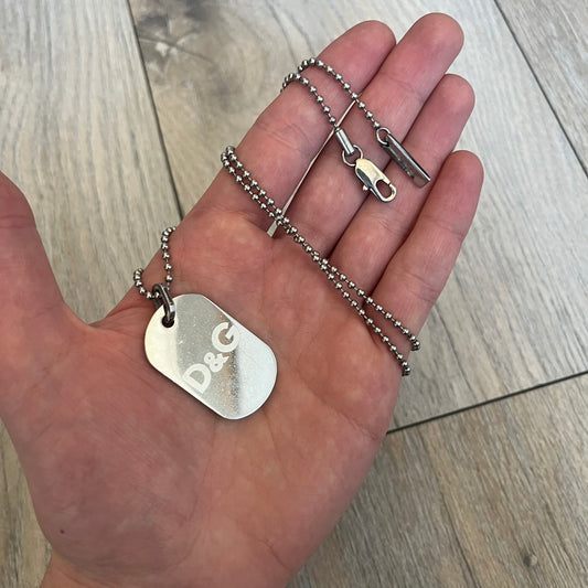 Dolce & Gabbana plain logo dog tag necklace in silver-tone stainless steel, featuring the iconic D&G logo engraved on a sleek tag. Suspended on a classic ball chain with a regulated size. A versatile accessory that combines minimal branding with everyday wearability.
