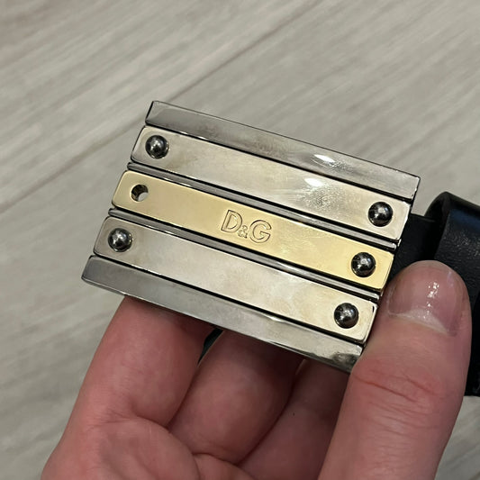 Dolce & Gabbana 2000s Silver/Gold Bars Belt crafted from black leather with a solid metal buckle plate. The buckle features three horizontal metal bars secured with visible screws, with silver-tone bars on the top and bottom and a gold-tone center bar engraved with the D&G logo. Finished with a structured leather strap, comes with the original dustbag.