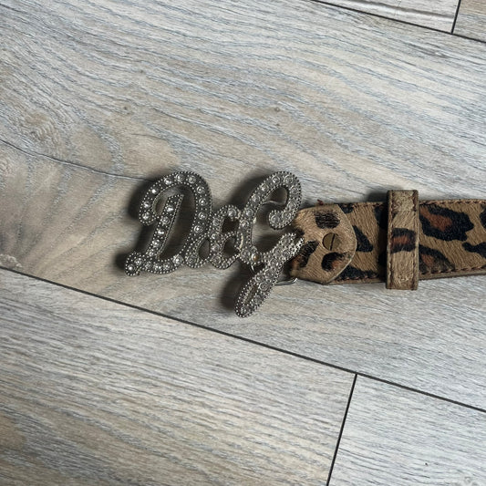 Dolce & Gabbana 2000s Studded Buckle Leopard Print Belt is a beige belt with an all-over leopard print and a short hair-textured exterior. The buckle features an italic-style D&G logo in a silver-tone finish with rhinestone detailing. The interior is finished in brown leather.