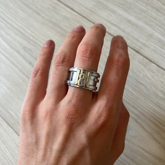 Dolce & Gabbana 3D logo ring crafted in silver-tone metal with a unique two-part construction. The base is a classic band, topped with a raised layer that wraps the D&G logo around the ring. Designed with a movable top section that spins, it’s a dynamic accessory merging playful function with signature branding.